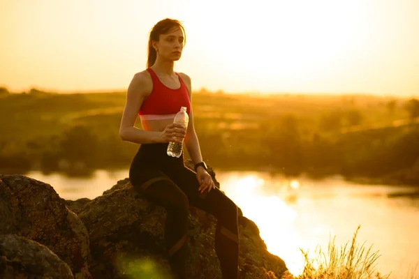 Mulher descansando e bebendo água depois de correr ao ar livre. Treino no pôr-do-sol quente do verão. Esporte e Vida Ativa Saudável . — Fotografia de Stock