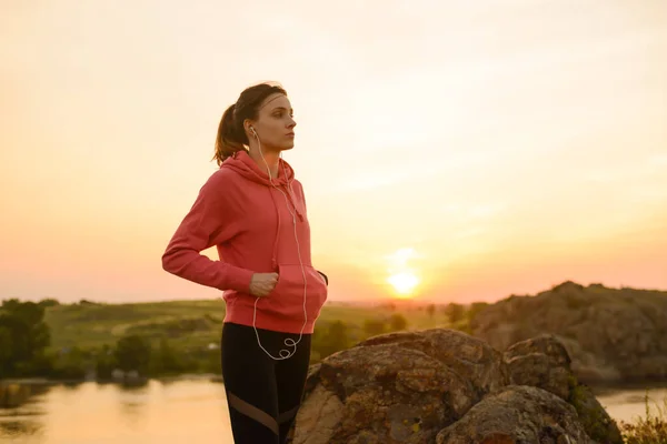 Kadın Koşucu idmandan sonra dinleniyor ve Sunset on the Rock 'ta müzik dinliyor. Spor Konsepti. — Stok fotoğraf