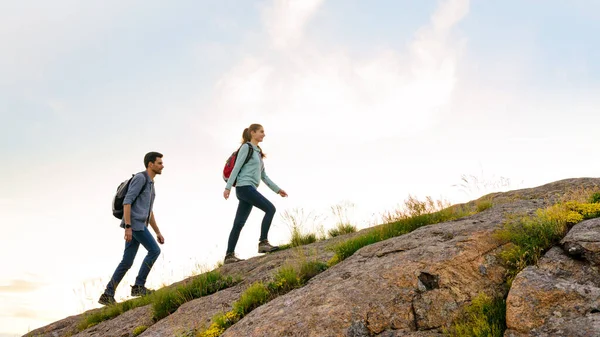 Couple of Young Happy Travelers Hiking with Backpacks on the Rocky Trail at the Evening. Family Travel and Adventure — Stock Photo, Image