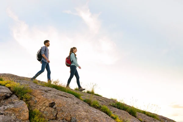 Couple of Young Happy Travelers Hiking with Backpacks on the Rocky Trail at the Evening. Family Travel and Adventure — Stock Photo, Image