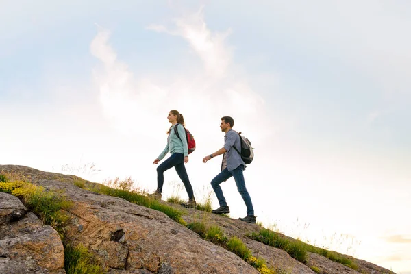 Couple of Young Happy Travelers Hiking with Backpacks on the Rocky Trail at the Evening. Family Travel and Adventure — Stock Photo, Image