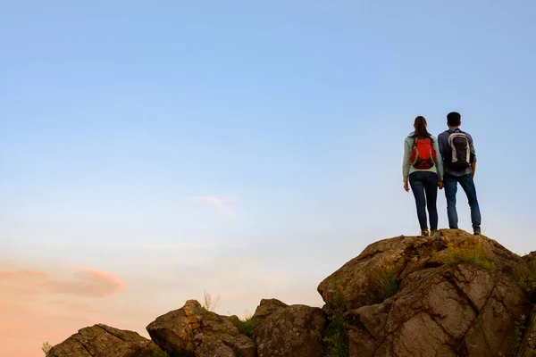 Ein Paar junger Reisender, die bei Sonnenuntergang auf dem Gipfel des Felsens stehen. Familienreise- und Abenteuerkonzept — Stockfoto