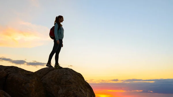 Joven viajera con mochila de pie en la cima de la roca al atardecer de verano. Concepto de viaje y aventura . — Foto de Stock