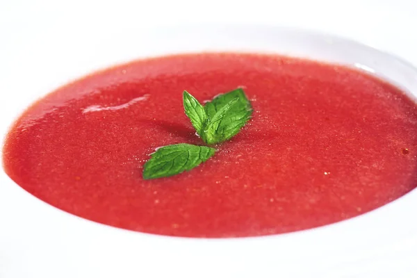 Primer plano de un plato de sopa de gazpacho con rodajas de tomate, pepino y cebolla, con hojas de menta — Foto de Stock