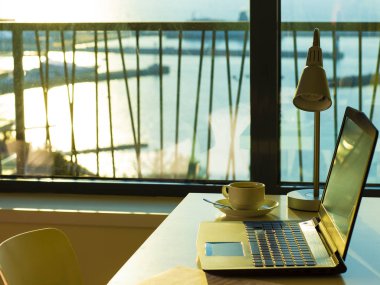Computer laptop and cup of coffee on the table inside modern room, which located close the sea beach clipart