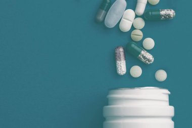 Çeşitli ilaç hapları, haplar, kapsüller ve mavi arka planda şişe..