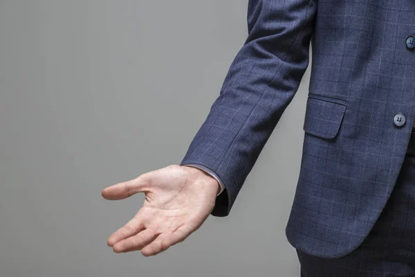 Empresário com braço para fora em um gesto acolhedor sobre fundo cinza — Fotografia de Stock