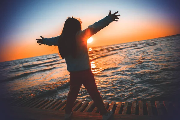 Gün doğumunda sahilde el kaldıran siluet kız. — Stok fotoğraf