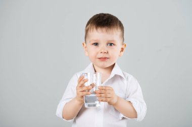 Küçük çocuk gri arka plan üzerinde camdan su içme