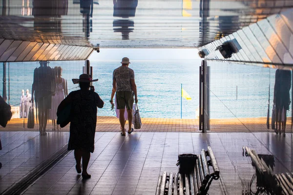 Silhouettes of older tourists going to the sea beach in the tunnel