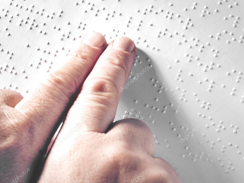Hands of a blind person reading some braille text touching the relief.