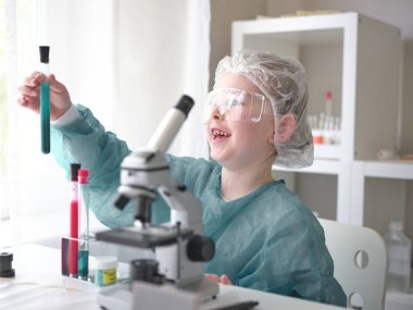 Evdeki masasında mikroskoba bakan sevimli küçük kız. Genç bilim adamı laboratuarında deneyler yapıyor.. 