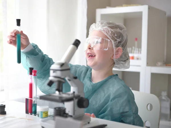 Słodka dziewczynka patrząc w mikroskop w jego biurku w domu. Młody naukowiec przeprowadzający eksperymenty w swoim własnym laboratorium. — Zdjęcie stockowe