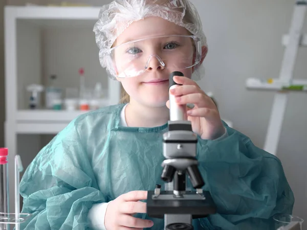 Roztomilá holčička se dívá do mikroskopu u jeho stolu doma. Mladý vědec provádí experimenty ve své domácí laboratoři. — Stock fotografie