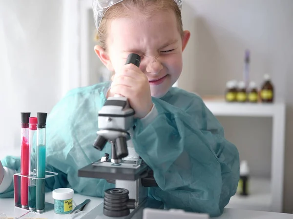 Linda niñita mirando al microscopio en su escritorio en casa. Joven científico haciendo experimentos en su laboratorio en casa . Imágenes de stock libres de derechos