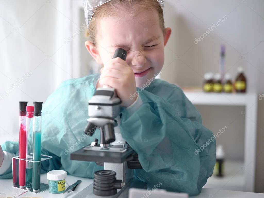 Cute little girl looking into microscope at his desk at home. Young scientist making experiments in his home laboratory. 