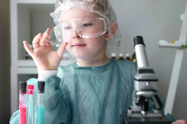Roztomilá holčička se dívá do mikroskopu u jeho stolu doma. Mladý vědec provádí experimenty ve své domácí laboratoři. — Stock fotografie