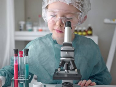 Evdeki masasında mikroskoba bakan sevimli küçük kız. Genç bilim adamı laboratuarında deneyler yapıyor.. 