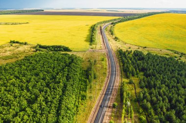 Sonbaharda gün batımında dağ vadisindeki yol manzarası. Asfalt yol manzarası, araba, turuncu otlu tepeler, mavi gökyüzü, ağaçlar, binalar. Otoyol ve tarlalar sonbaharda.