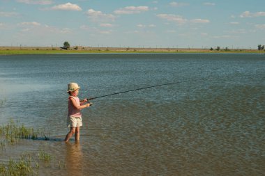 Bir yaz gününde elinde oltayla nehirde balık tutan küçük bir kız.