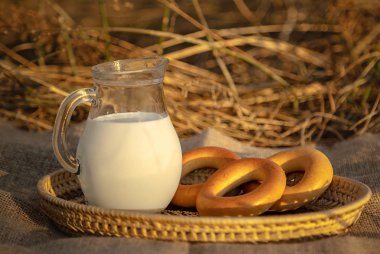 Süt sürahi, simit, kuru çim yakın çekim bir arka plan üzerinde bir hasır sepet içinde