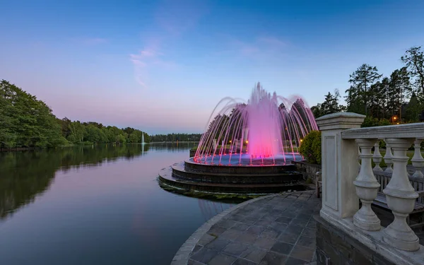 在公园美丽的傍晚湖岸边照明的豪华喷泉 — 图库照片