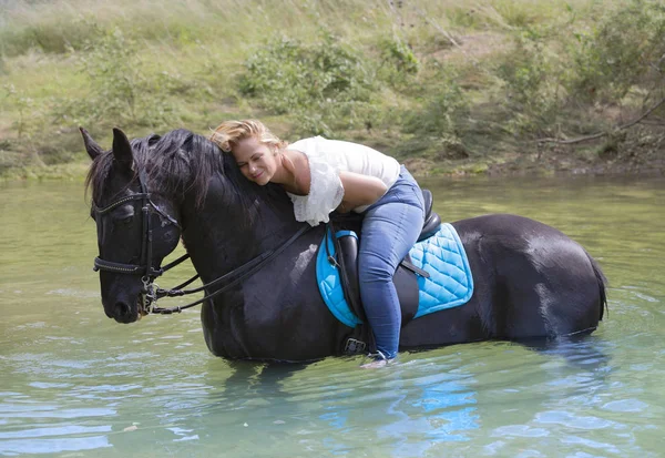 女性ライダーと彼女の黒い馬が川で歩いています — ストック写真