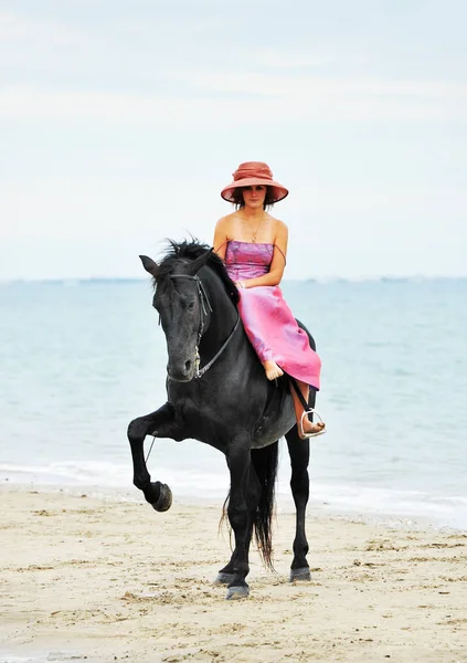 骑马的女孩和她的黑种马在海滩上 — 图库照片