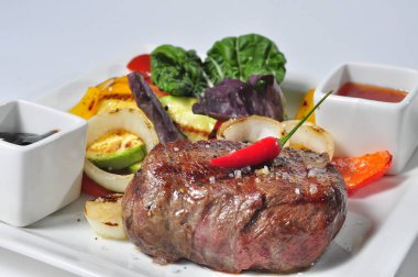 Sebzeli biftek ve beyaz tabakta servis edilen sos.