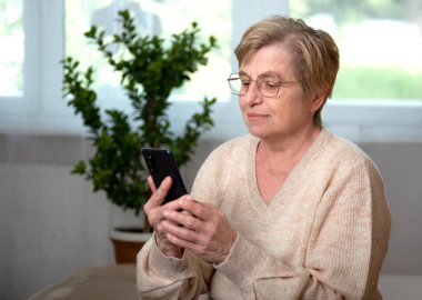 Akıllı telefonu olan yaşlı bir kadın mutlu bir gülümsemeyle telefona cevap veriyor.