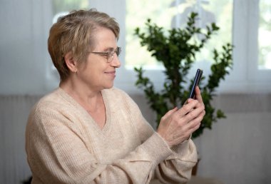 Akıllı telefonu olan yaşlı bir kadın mutlu bir gülümsemeyle telefona cevap veriyor.