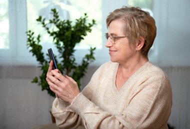 Akıllı telefonu olan yaşlı bir kadın mutlu bir gülümsemeyle telefona cevap veriyor.