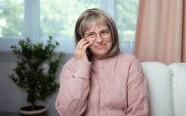 Akıllı telefonu olan yaşlı bir kadın mutlu bir gülümsemeyle telefona cevap veriyor.