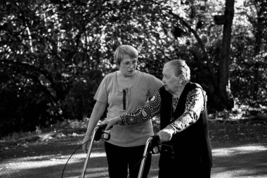 Yürüyen ve yardım alarak parkta yürüyüş yapan yaşlı bir kadın.