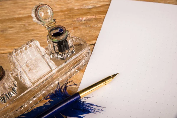 Dip pen in the shape of a quill on a document and next to an ink well