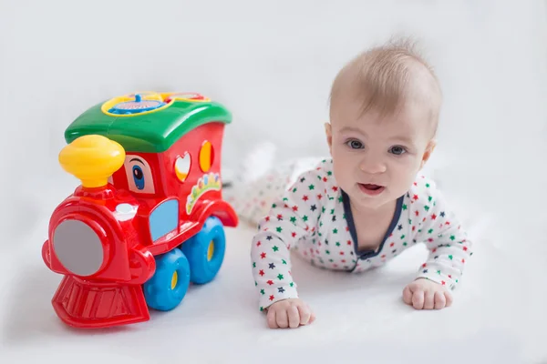 Babyjongen liggen met speelgoed trein op wit — Stockfoto