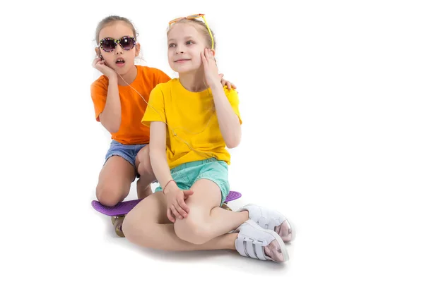Two girls listenning to the music and sitting on skateboard over — Stock Photo, Image