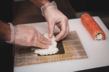 Şefin ellerinin, siyah sırtında suşi rulosu için pirinç hazırlarken kısmi görüntüsü.