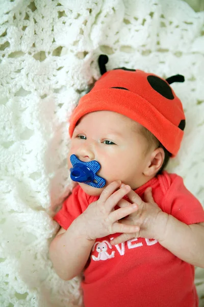 Το μωρό στο στήθος σε κόκκινο bodykit και κόκκινο καπάκι με κέρατα στο τα λεμονάτα — Φωτογραφία Αρχείου