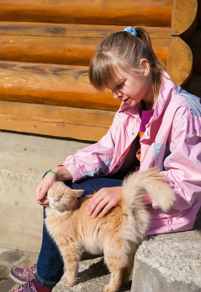 Linda chica adolescente en una chaqueta rosa acaricia a un gato rojo contra la ba —  Fotos de Stock