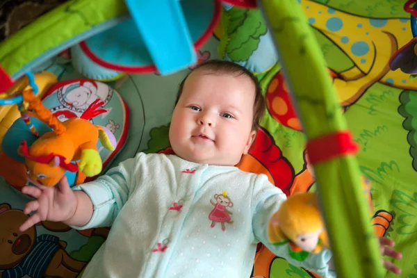 Šest měsíců stará holčička se rozkládá na mnohobarevný vyvíjecí koberec — Stock fotografie