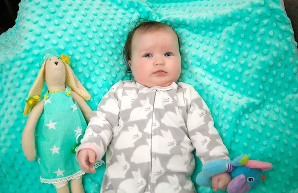 Niña de 6 meses acostada en una alfombra brillante de menta con un ruido —  Fotos de Stock