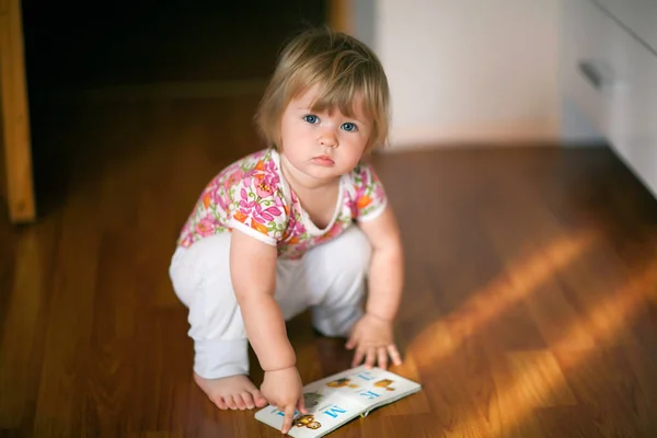 Маленька дівчинка в квітковій футболці сидить на підлозі, дивлячись на — стокове фото