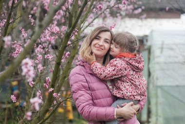 Anne kollarında pembe Kurtkaz giymiş bir kızı tutuyor.