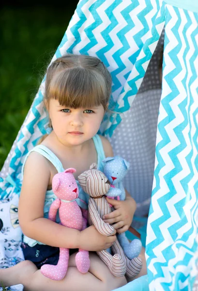 かわいい女の子がおもちゃを持って通りの夏にファブリックハウスに座っている ストック画像