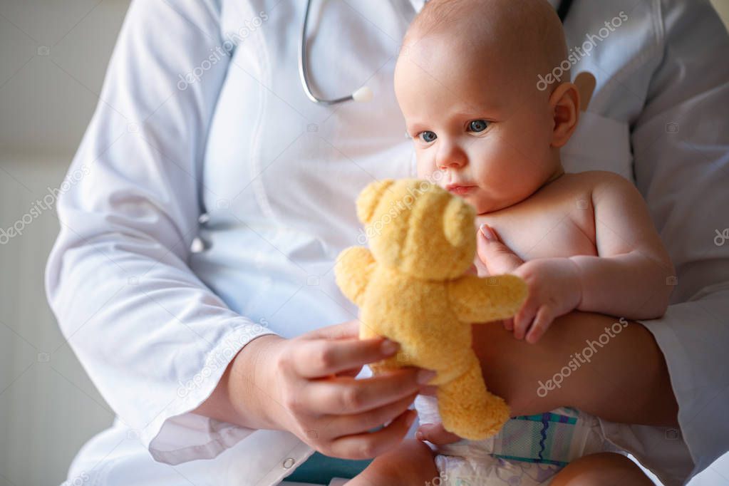 Little boy looking in yellow teddy bear in pediatrician's lap 