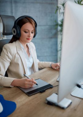 Kulaklıklar giyen ve kalem masada çalışan genç kadın