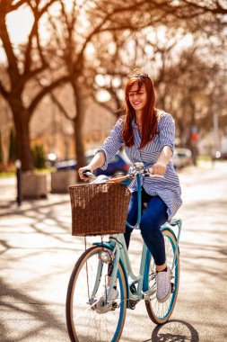 Güzel gülümseyen zencefil kız parkta bisiklete biniyor