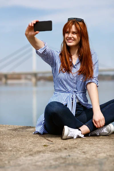 Jovem Fêmea Sentada Areia Junto Rio Fazendo Selfie — Fotografia de Stock