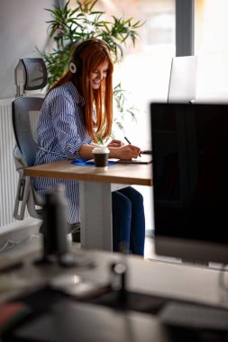 Kulaklıklar ile ofiste çalışan genç kadın grafik tasarımcı